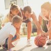 Família a brincar com uma bola de basquetebol num campo exterior, com expressões de alegria e envolvimento de todos os elementos.