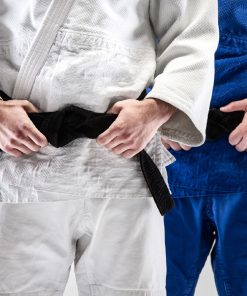 Dois praticantes de artes marciais com quimonos, um branco e outro azul, com cintos pretos, focando-se na zona do tronco e das mãos a ajustar o cinto.