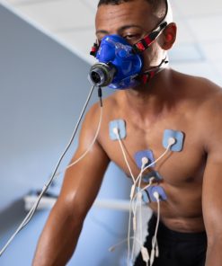 Homem a realizar um teste de esforço com máscara de medição de consumo de oxigénio e vários elétrodos colocados no peito, ligado a equipamento de monitorização fisiológica.