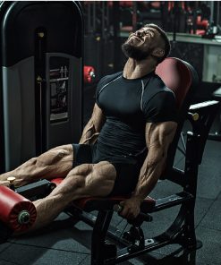 Homem musculado a treinar numa máquina de extensão de pernas no ginásio, com expressão de esforço e foco, vestindo equipamento desportivo preto.