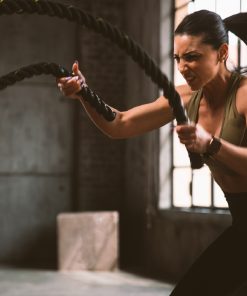 Mulher em treino funcional com cordas de resistência, demonstrando intensidade, força e foco num ambiente de ginásio industrial.