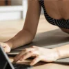 Mulher em roupa de treino a utilizar tablet sobre colchão de exercício.