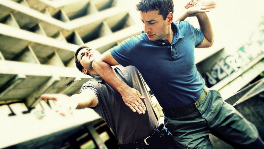 Dois homens a praticar técnicas de Krav Maga, em ambiente citadino, ilustrando treino de combate corpo a corpo e autodefesa.