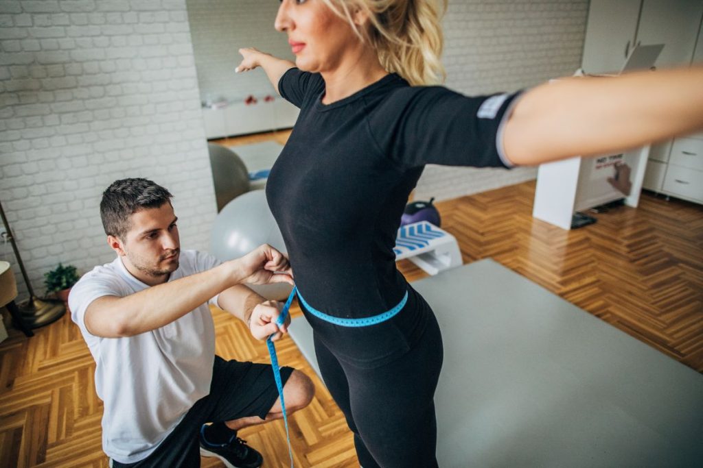 Personal Trainer a fazer avaliação física, nomeadamente a medir a cintura a uma mulher