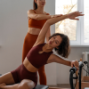 Instrutora de pilates orienta aluna em exercício de alongamento, promovendo flexibilidade, postura e equilíbrio num estúdio calmo e luminoso.